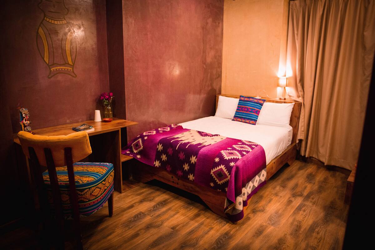 A room with a bed, a wooden desk, a chair, and a wall with a mural.