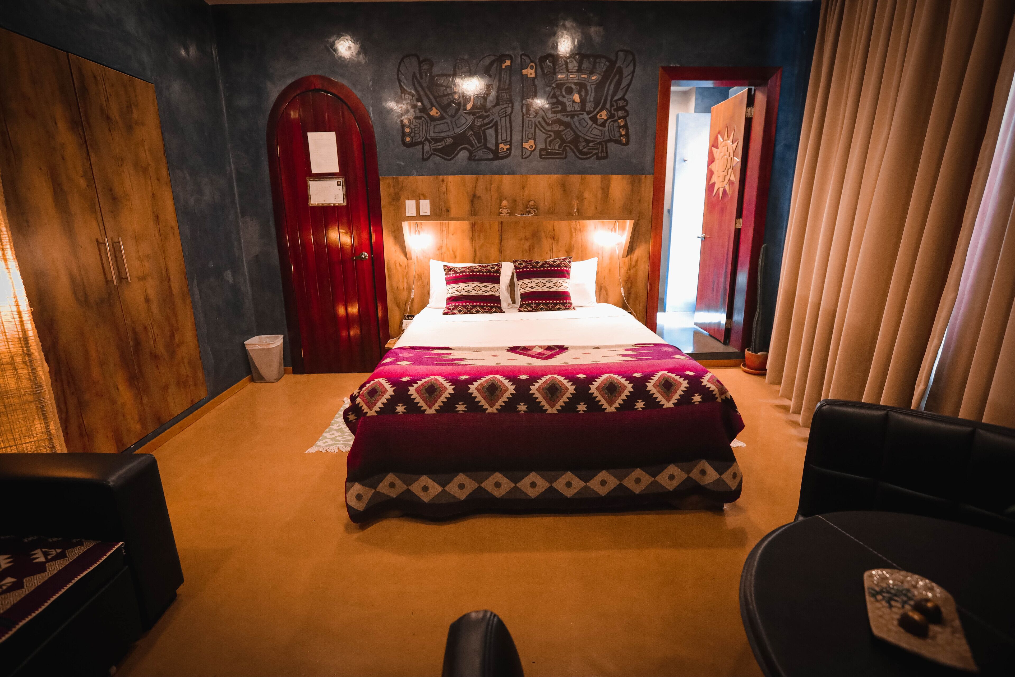 A hotel room with a large bed, a wooden wardrobe, a red door, and a view of the outside.