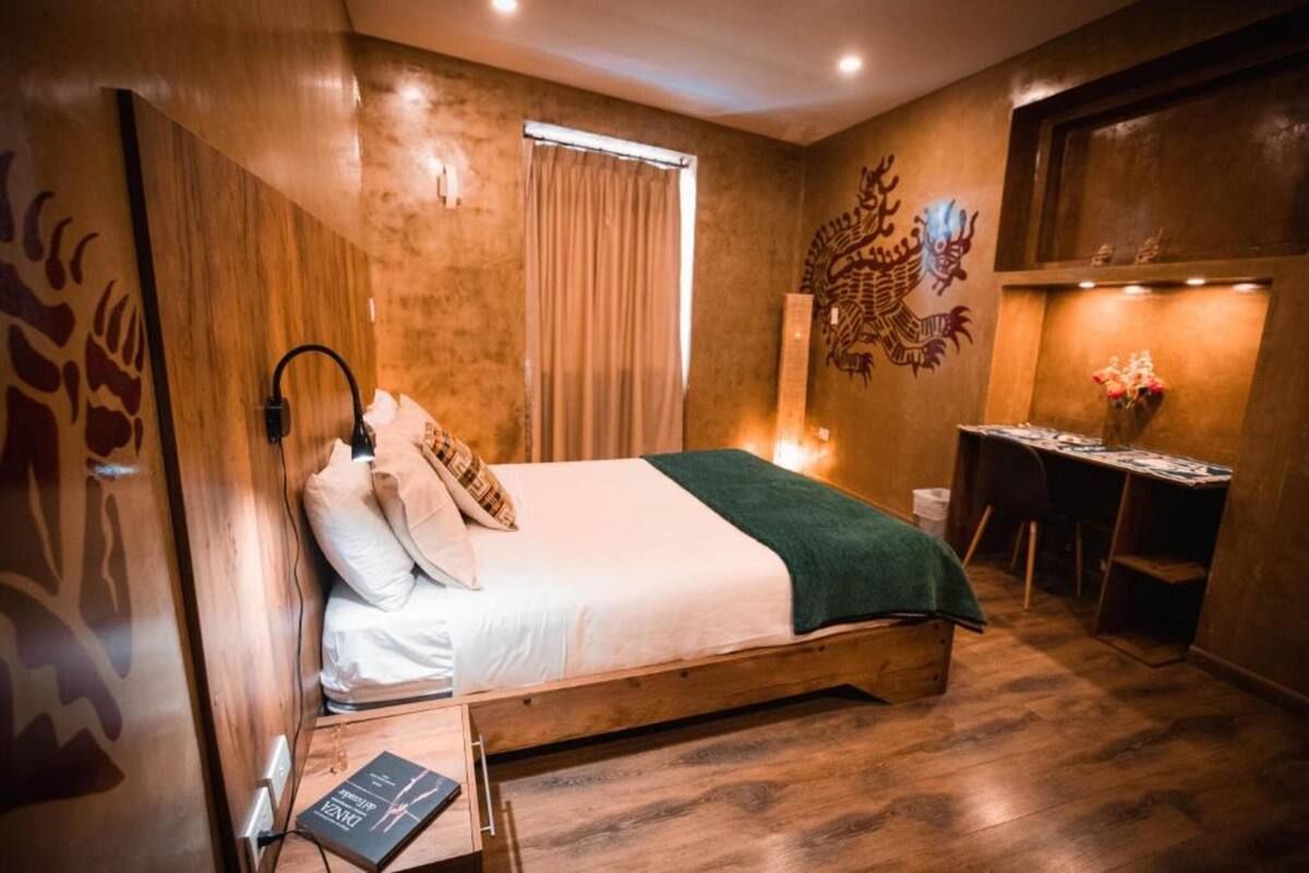 A bedroom with a wooden bed, a desk, a chair, and a decorative wall piece.