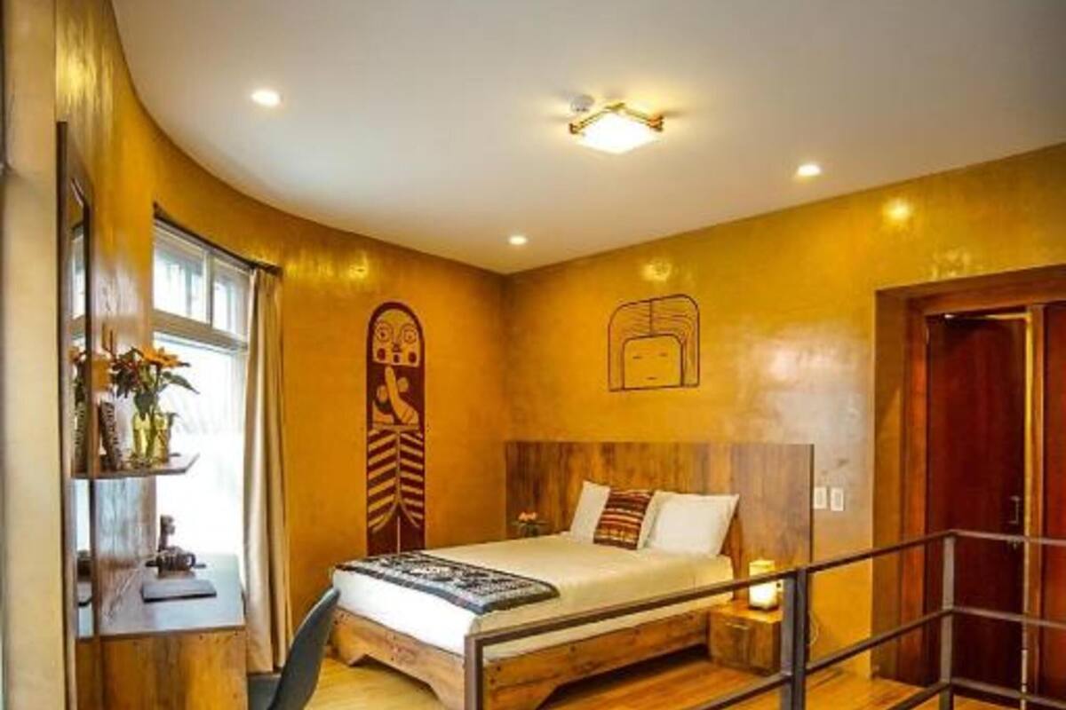 A bedroom with a bed, a desk, and a chair. There is a staircase leading to an upper level.