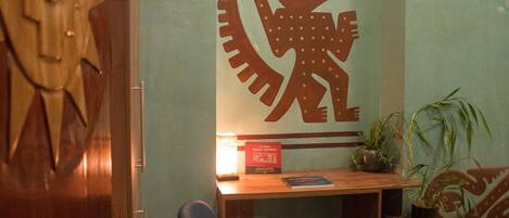 Una habitación con un escritorio de madera, una silla azul, un adorno en la pared y una planta en maceta.