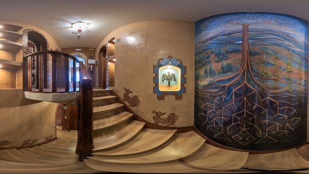 Una escalera de caracol con escalones de madera y elementos decorativos en la pared, incluyendo un mural de un árbol y patrones geométricos.
