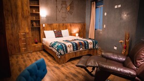Una cama de madera con un edredón colorido, un sillón de cuero y una pared con un adorno decorativo.