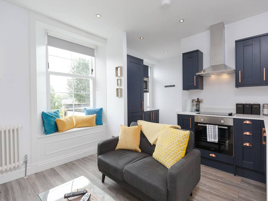 A modern kitchen with dark cabinets, a built-in oven, and a window with blue cushions.