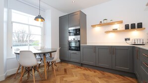 A modern kitchen with grey cabinets, a built-in oven, and a dining area with a round table and chairs. - Dollar Apartments at 41 (Dollar)