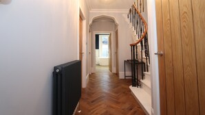 A hallway with a wooden floor, a radiator, a staircase with a wooden handrail, and a door. - Dollar Apartments at 41 (Dollar)