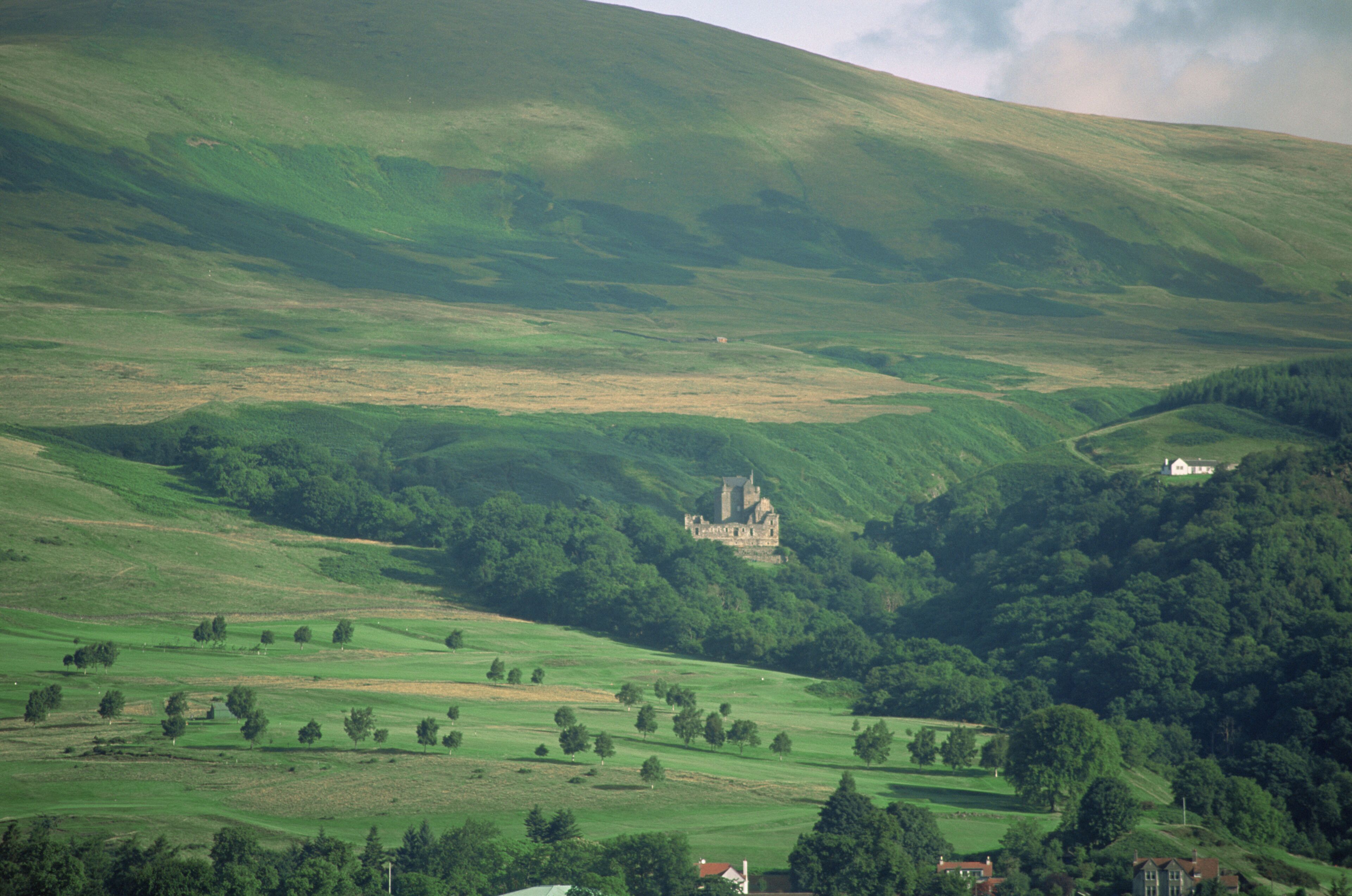 A castle on a hill with surrounding green fields and a few scattered trees.