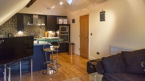 A modern kitchen with a central island, bar stools, and a wooden ceiling. - The Apartment No 2 The Old Red King Pub (Manchester)