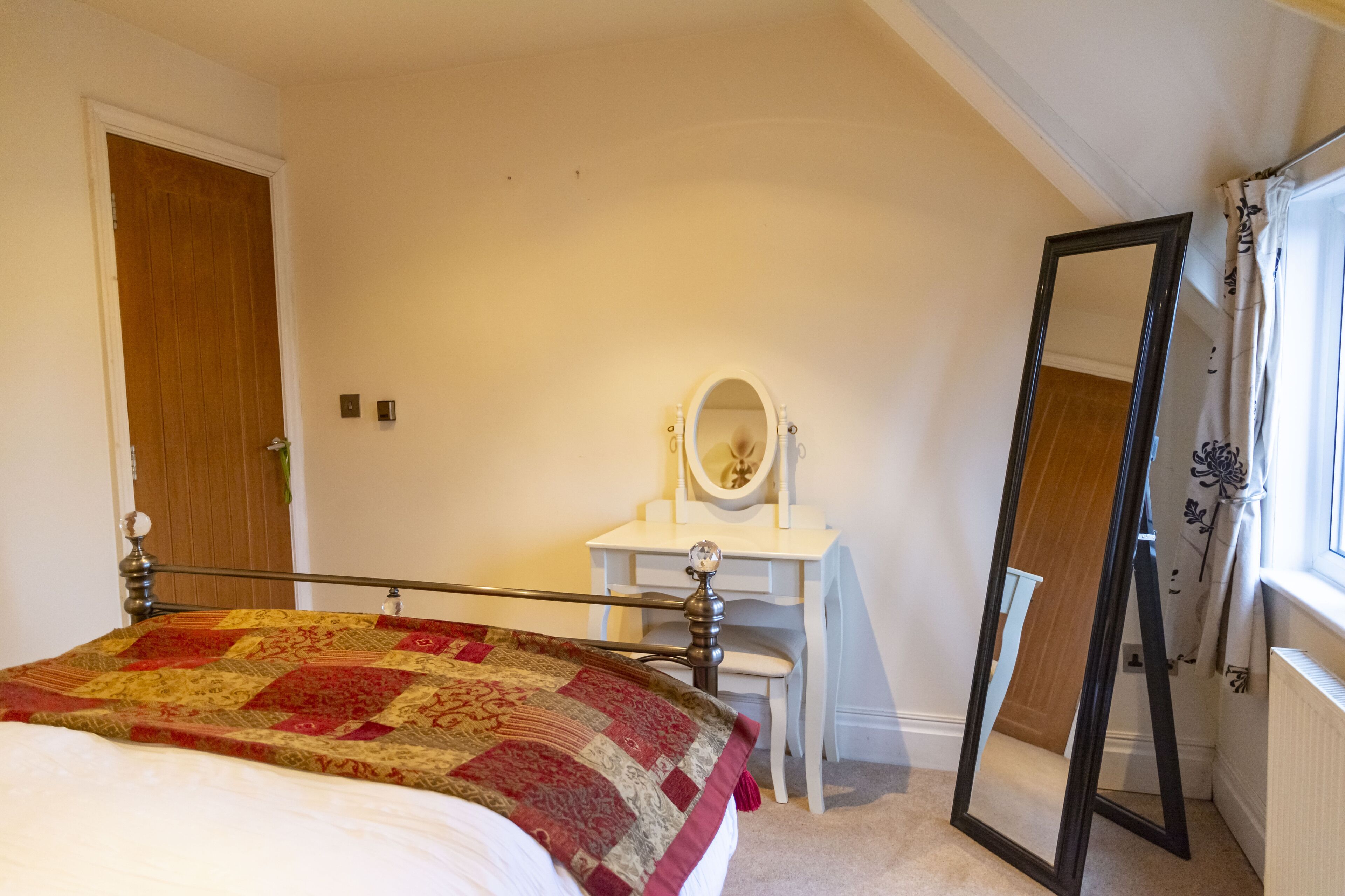 A bedroom with a bed, a desk with a mirror, and a wardrobe.