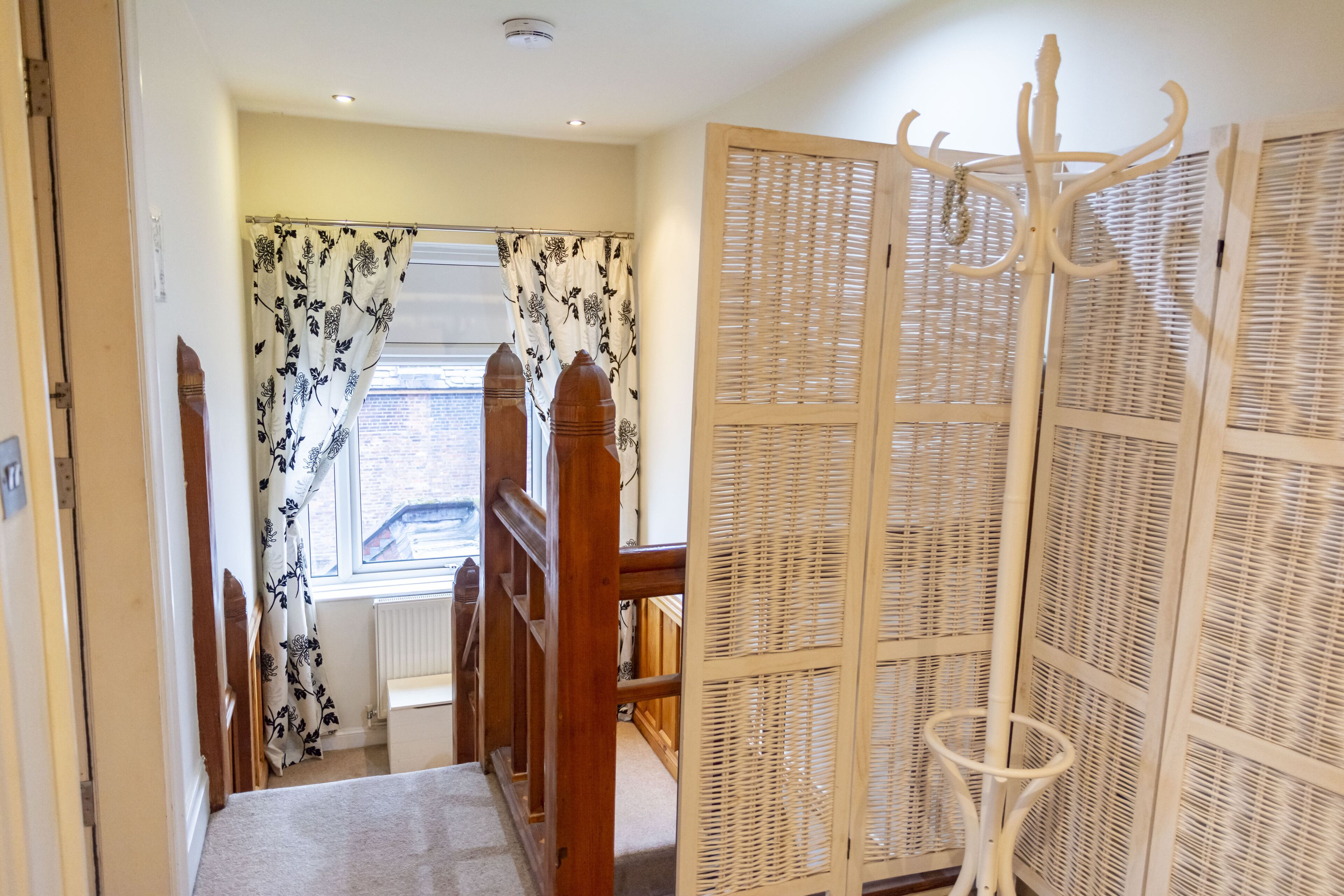 A staircase with a wooden handrail, a white radiator, and a window with patterned curtains.