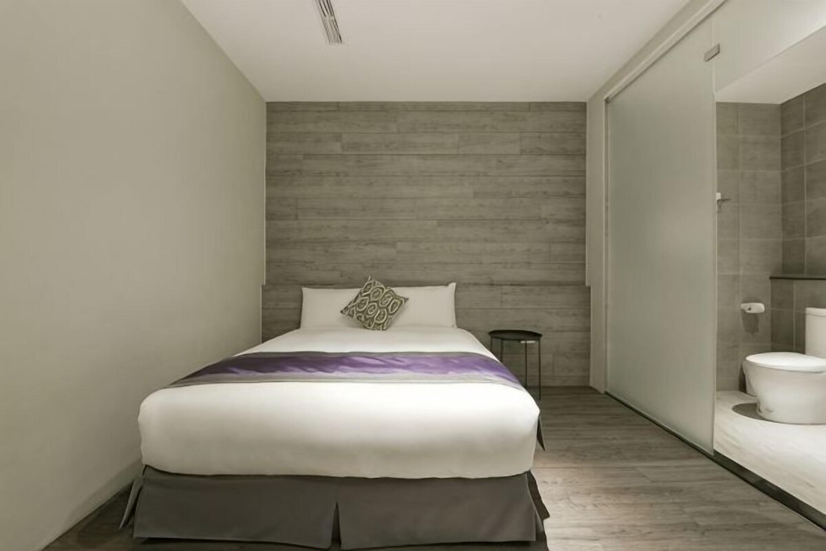 A modern bedroom with a bed, a bedside table, and a view into the bathroom.