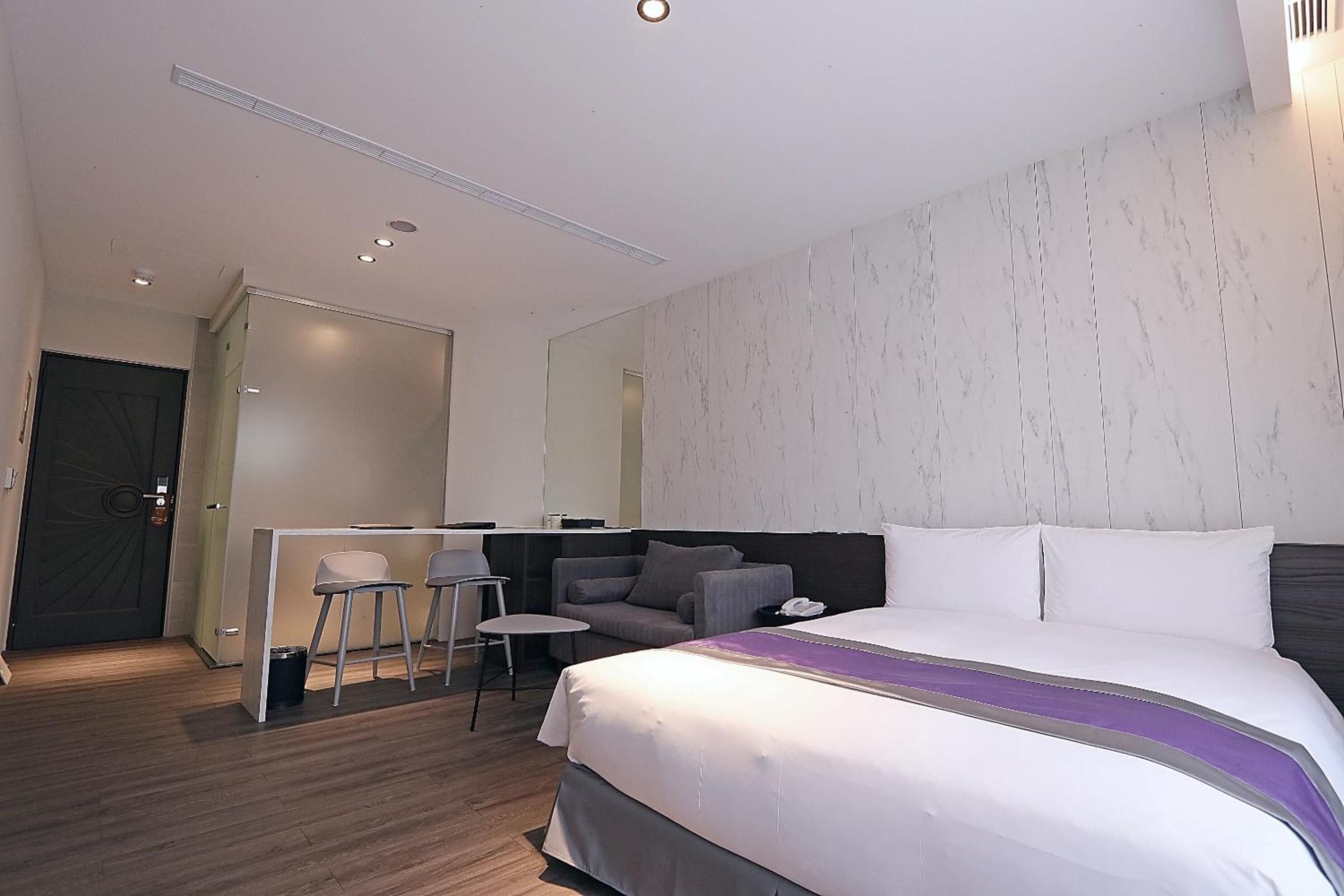 A modern hotel room with a large bed, a desk with two chairs, and a sofa.