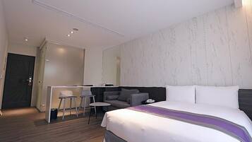 A modern hotel room with a large bed, a desk with two chairs, and a sofa.