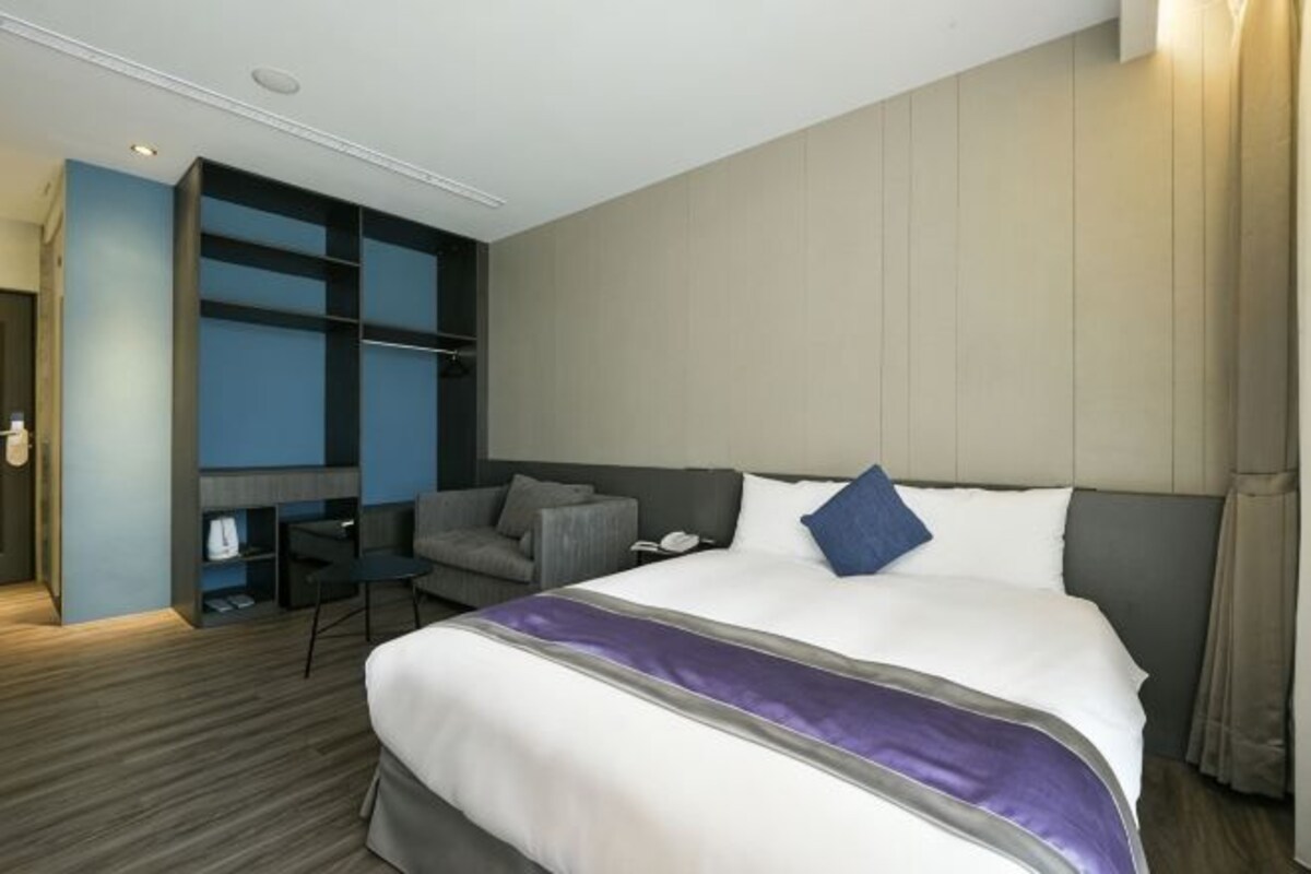 A hotel room with a large bed, a desk, and a seating area.