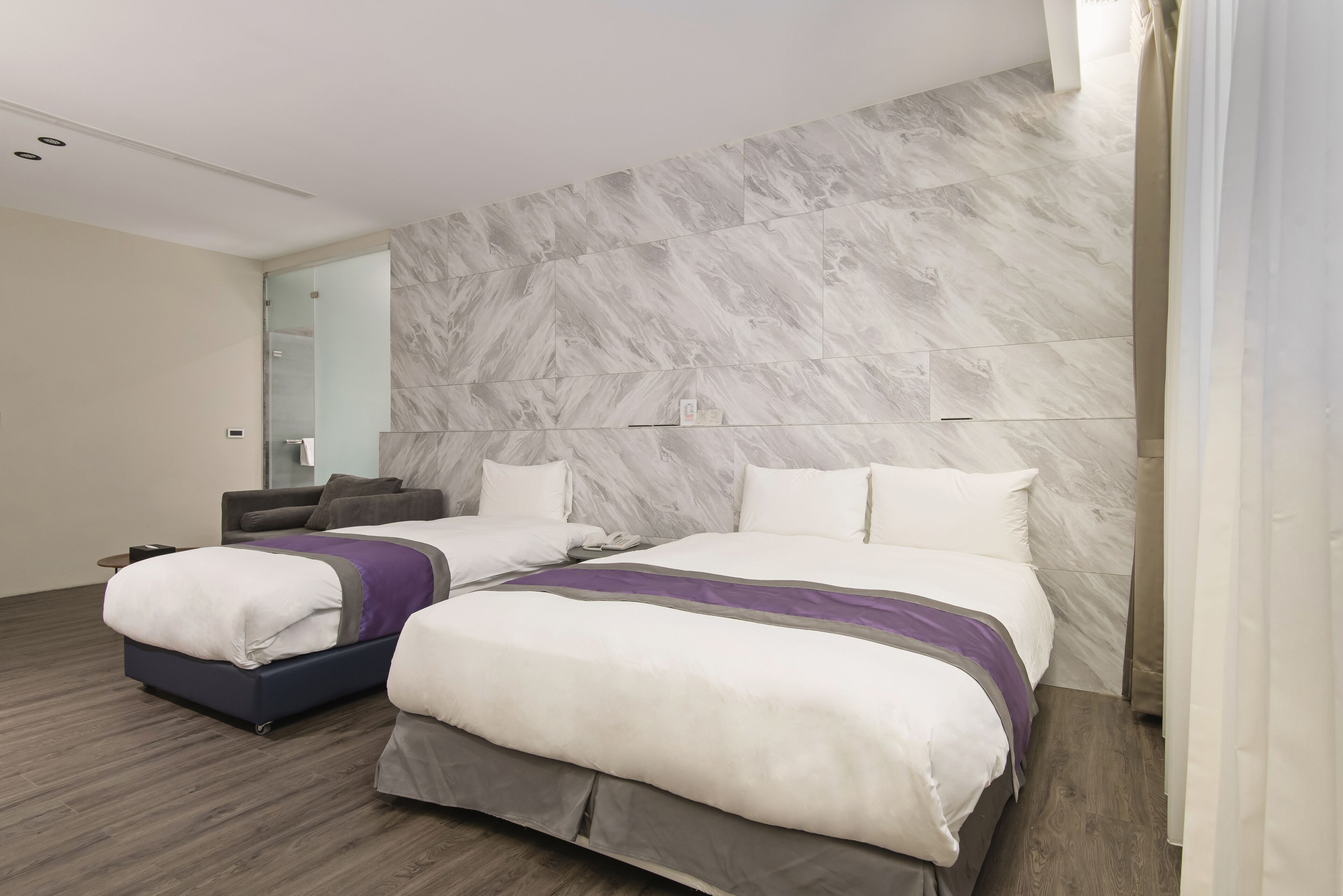 Una habitación de hotel moderna con una cama grande, otra más pequeña y un cabecero con diseño de mármol.