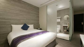 A hotel room with a bed, a nightstand, a bathroom with a toilet, and a mirror.