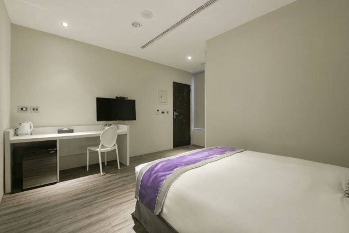 A hotel room with a bed, a desk, a chair, a television, and a door.