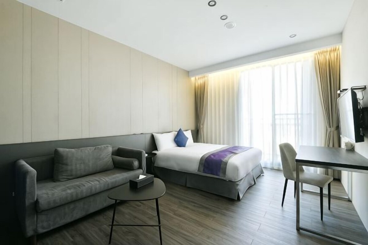 A hotel room with a bed, a sofa, a desk, and a chair.
