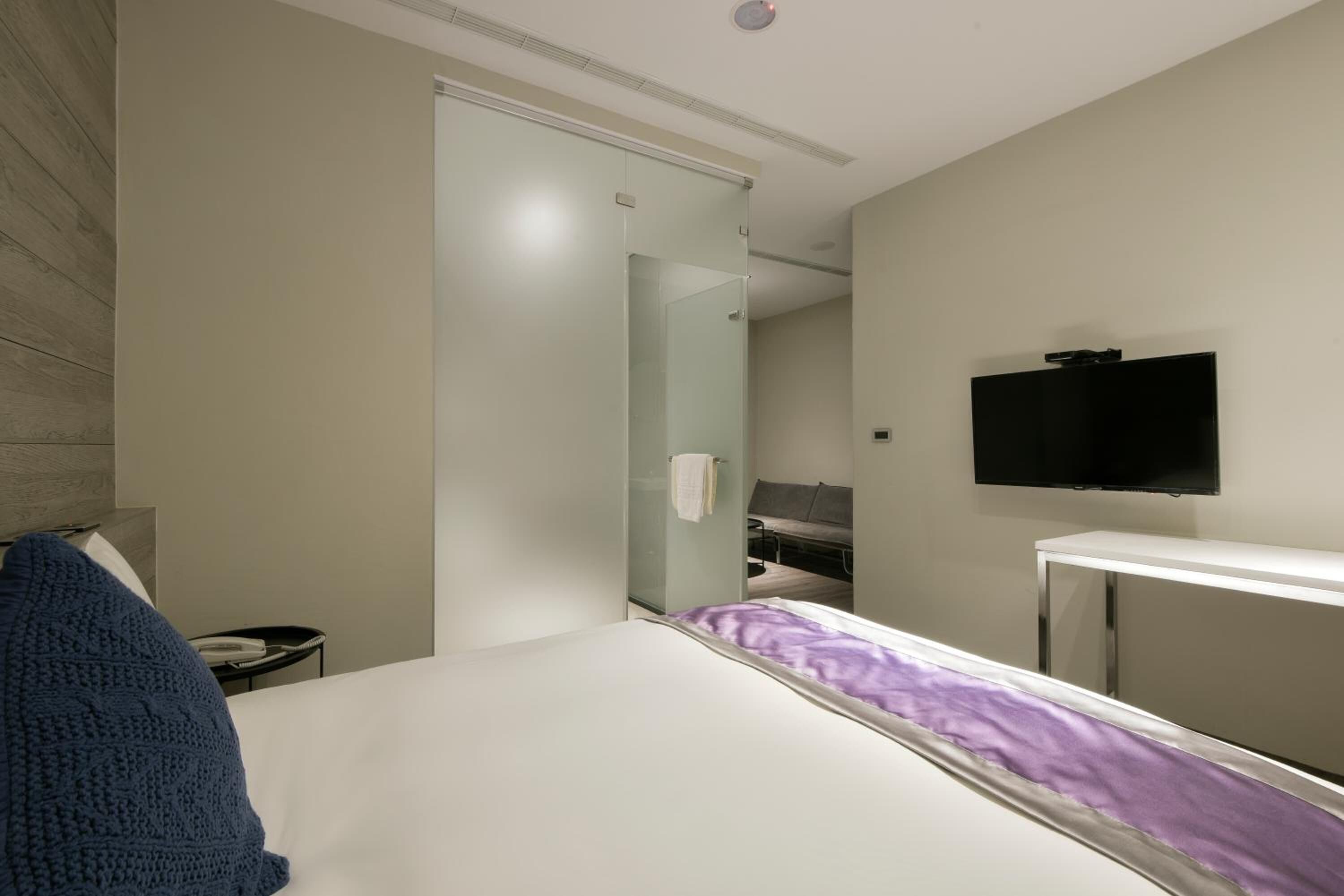 A modern hotel room with a bed, a television, and a glass partition wall.