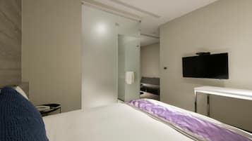 A modern hotel room with a bed, a television, and a glass partition wall.