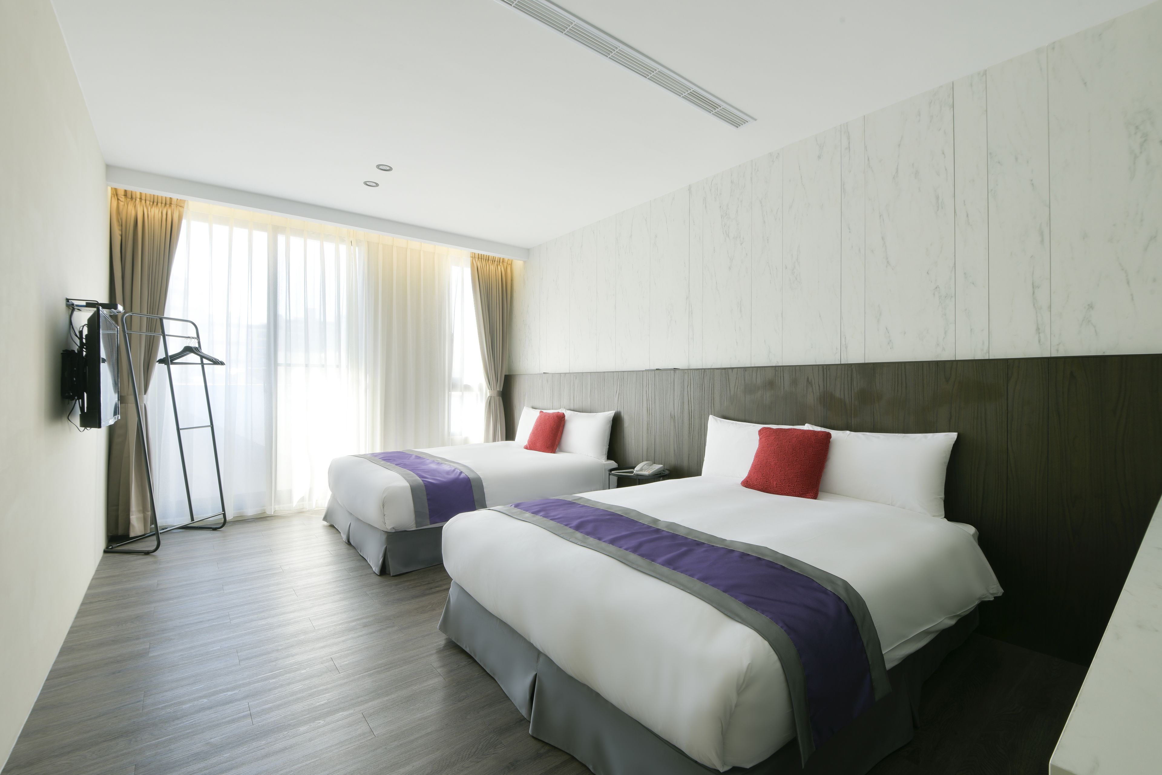 A hotel room with two beds, a wardrobe, a desk, and a window with curtains.