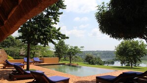 A pool area with lounge chairs and a view of a lake. - Holland Park (Kayunga)