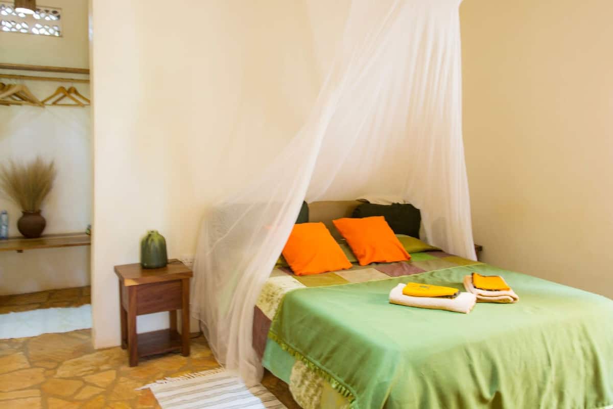 A bedroom with a bed under a canopy, a nightstand, and a potted plant.
