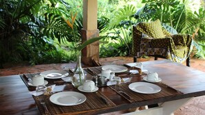A dining table set with plates, cups, and a vase, surrounded by lush greenery. - Holland Park (Kayunga)