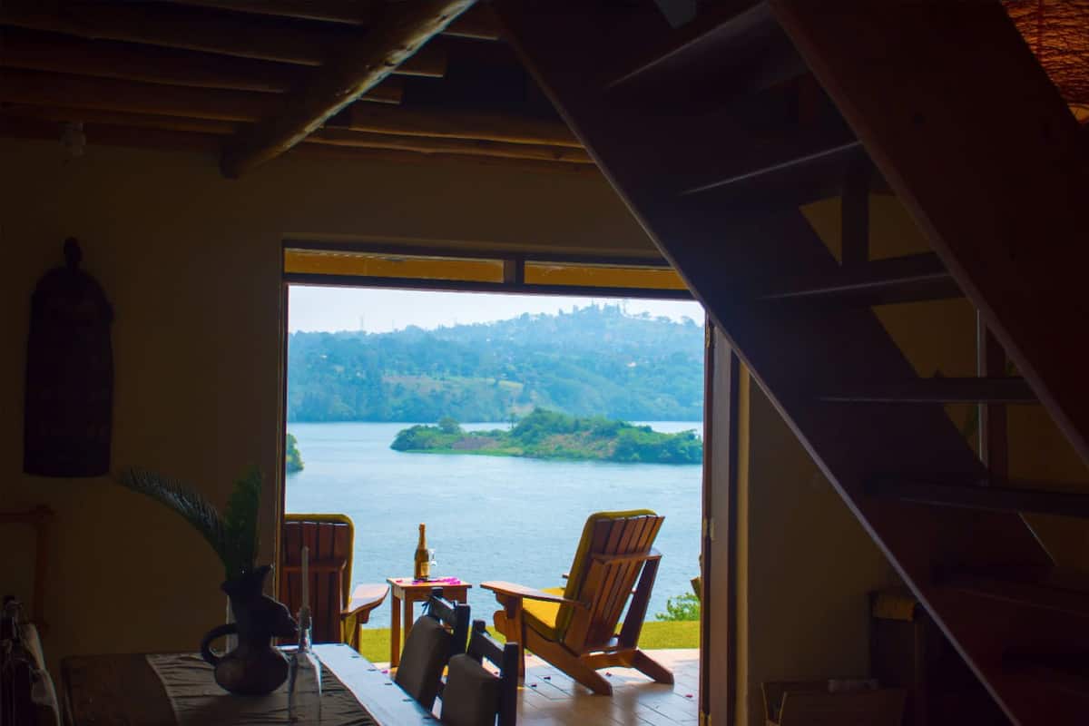 A room with a view of a lake, a wooden table with chairs, and a potted plant.