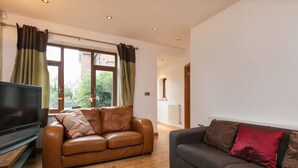 A living room with a brown leather sofa, a grey sofa, a flat-screen TV, and a window with curtains. - The Old Vicarage Lodge (Manchester)