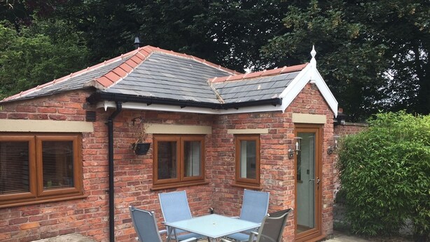 A small brick house with a tiled roof, a front door, and a patio with a table and chairs. - The Old Vicarage Lodge (Manchester)
