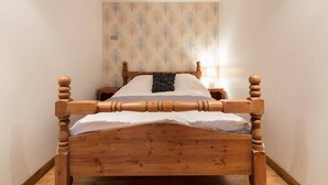 A narrow room with a wooden four-poster bed, a nightstand, and a wall-mounted lamp. - The Old Vicarage Lodge (Manchester)