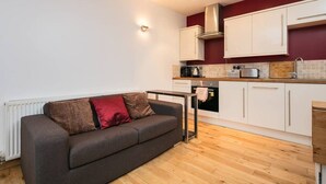 A compact living space with a kitchenette, a sofa with cushions, and a radiator. - The Old Vicarage Lodge (Manchester)