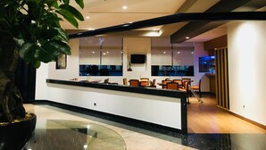 Un área de recepción moderna con una recepción de vidrio curvo, asientos y una planta grande en maceta.