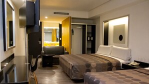 Habitación de hotel moderna con cama, escritorio, silla y una pequeña mesa. Hay un espejo en la pared y una puerta que da a otra habitación.