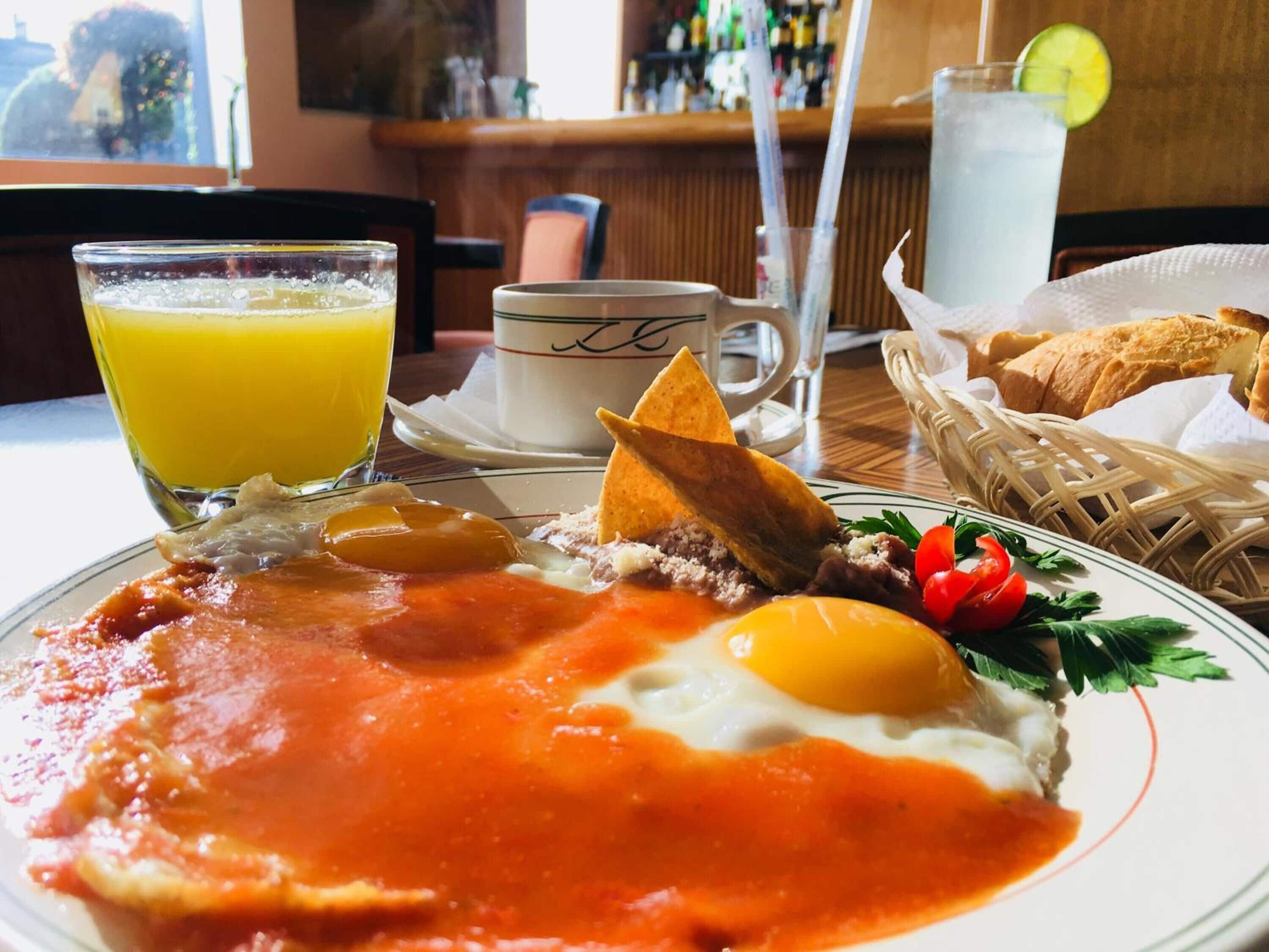 A breakfast plate with eggs, refried beans, and a side of toast, accompanied by a glass of orange juice and a cup of coffee.