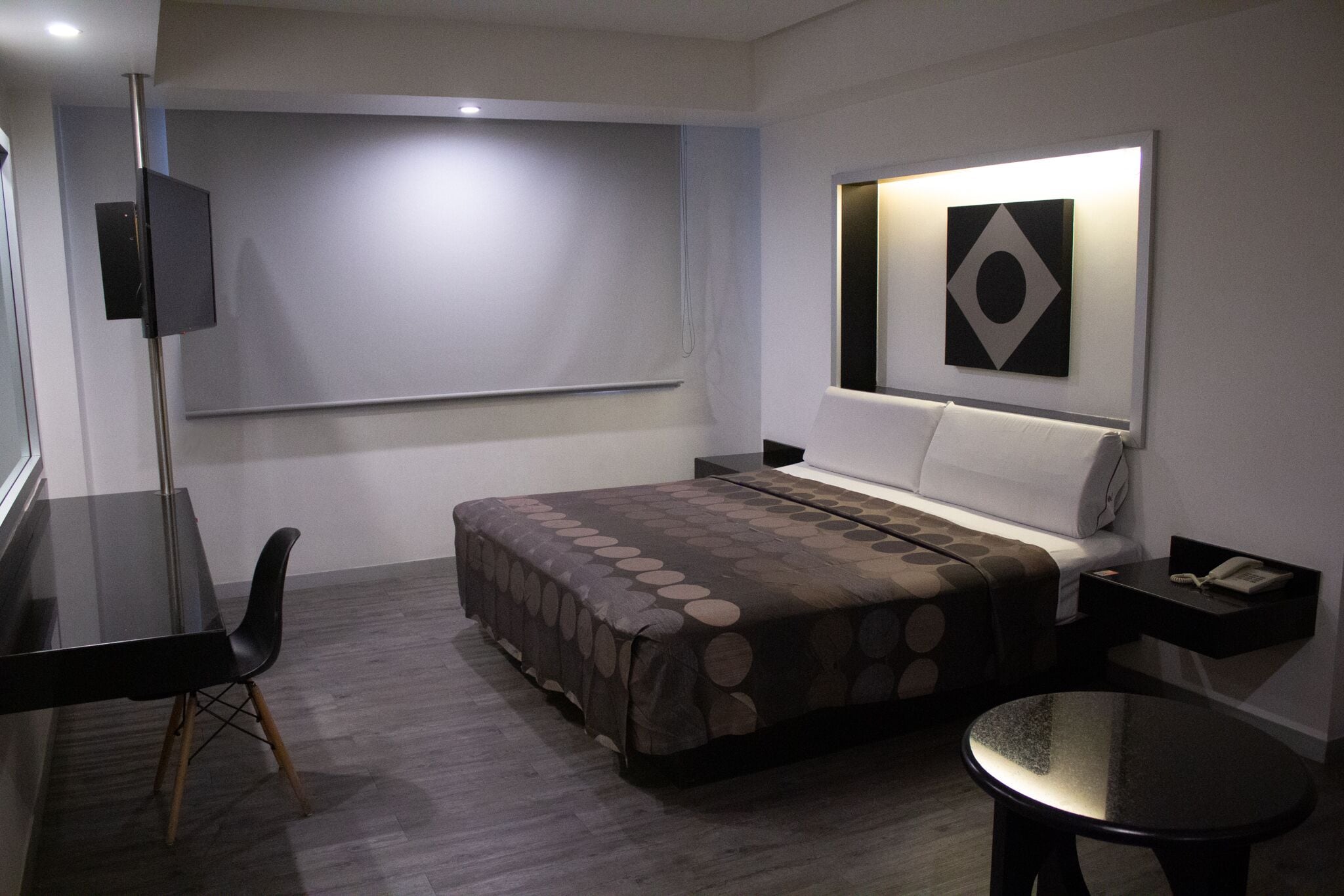 Habitación de hotel con cama, escritorio, silla, una mesita y televisor.