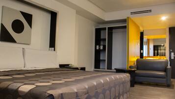 Una habitación de hotel moderna con una cama grande, un sofá gris y una obra de arte colgada en la pared.