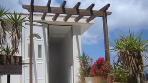 A white building with a wooden pergola entrance, potted plants, and a sign with numbers. - Kleio Studios (Platanias)