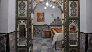 Una habitación con una cama, una mesita y un espejo. Hay un cuadro en la pared y un arco decorativo.