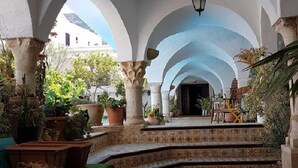 Un patio interior con arcos, plantas en macetas y suelo de baldosas.