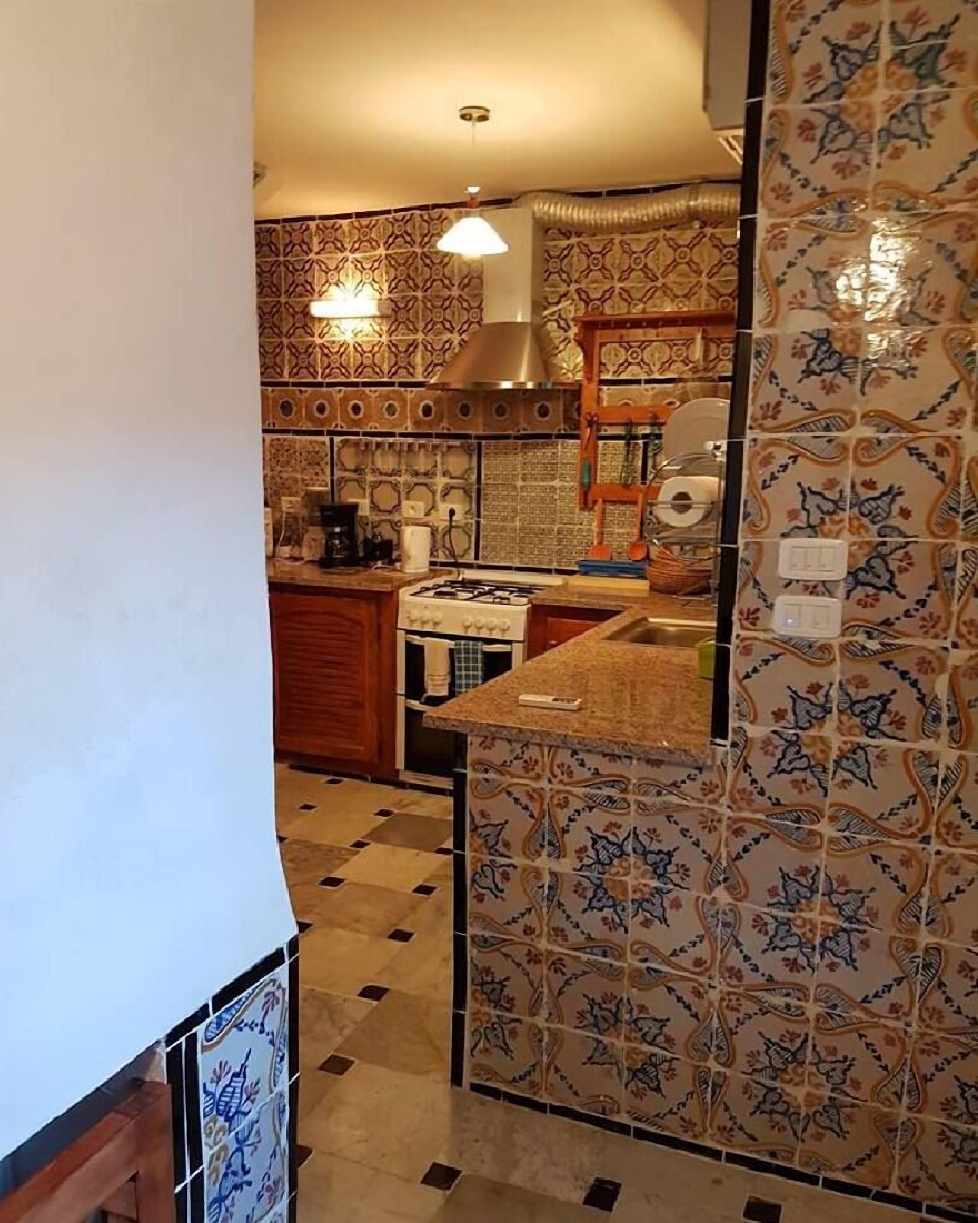 Una cocina con baldosas estampadas, una estufa a gas y un lavamanos.
