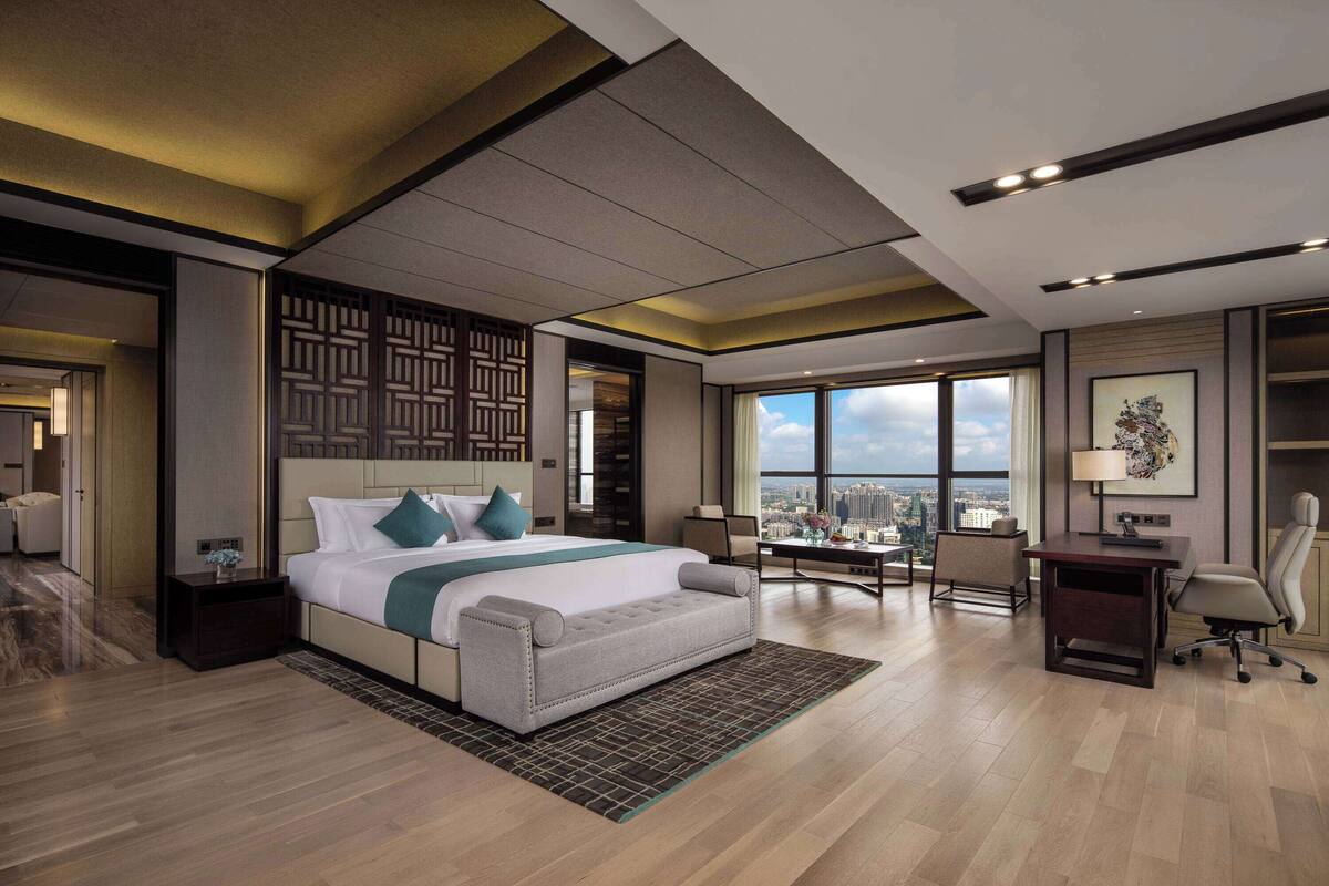 A modern hotel room with a large bed, a desk, and a view of the city.