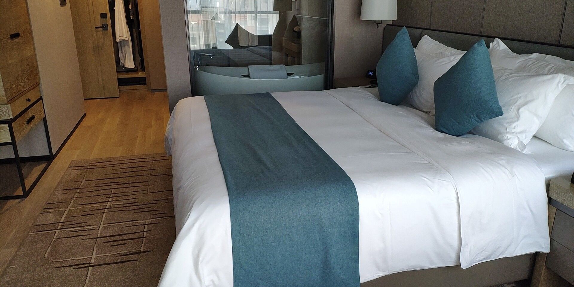 Een hotelkamer met een groot bed, een nachtkastje, een lamp en uitzicht op de stad.