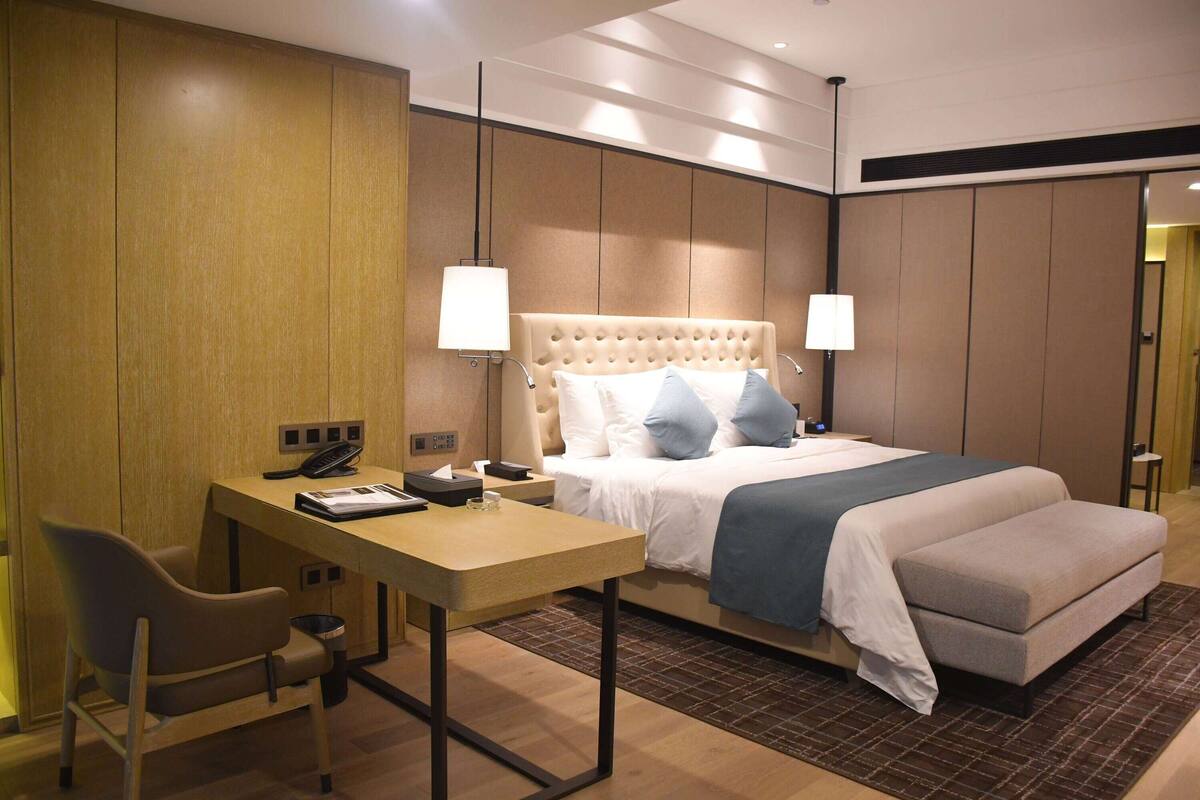 A hotel room with a bed, bedside tables, a desk, a chair, and a trash bin.
