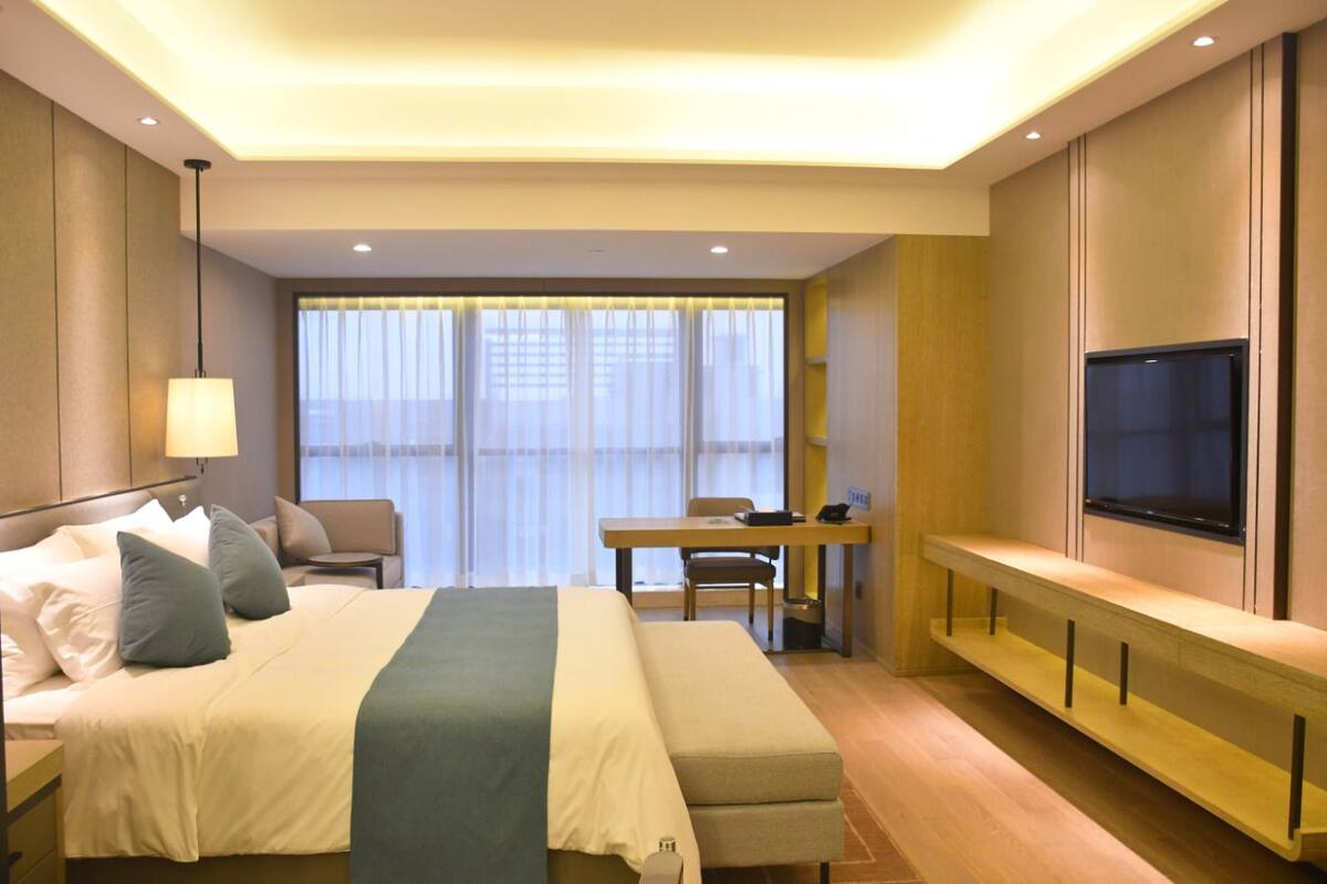 A hotel room with a bed, a desk, a chair, and a TV.