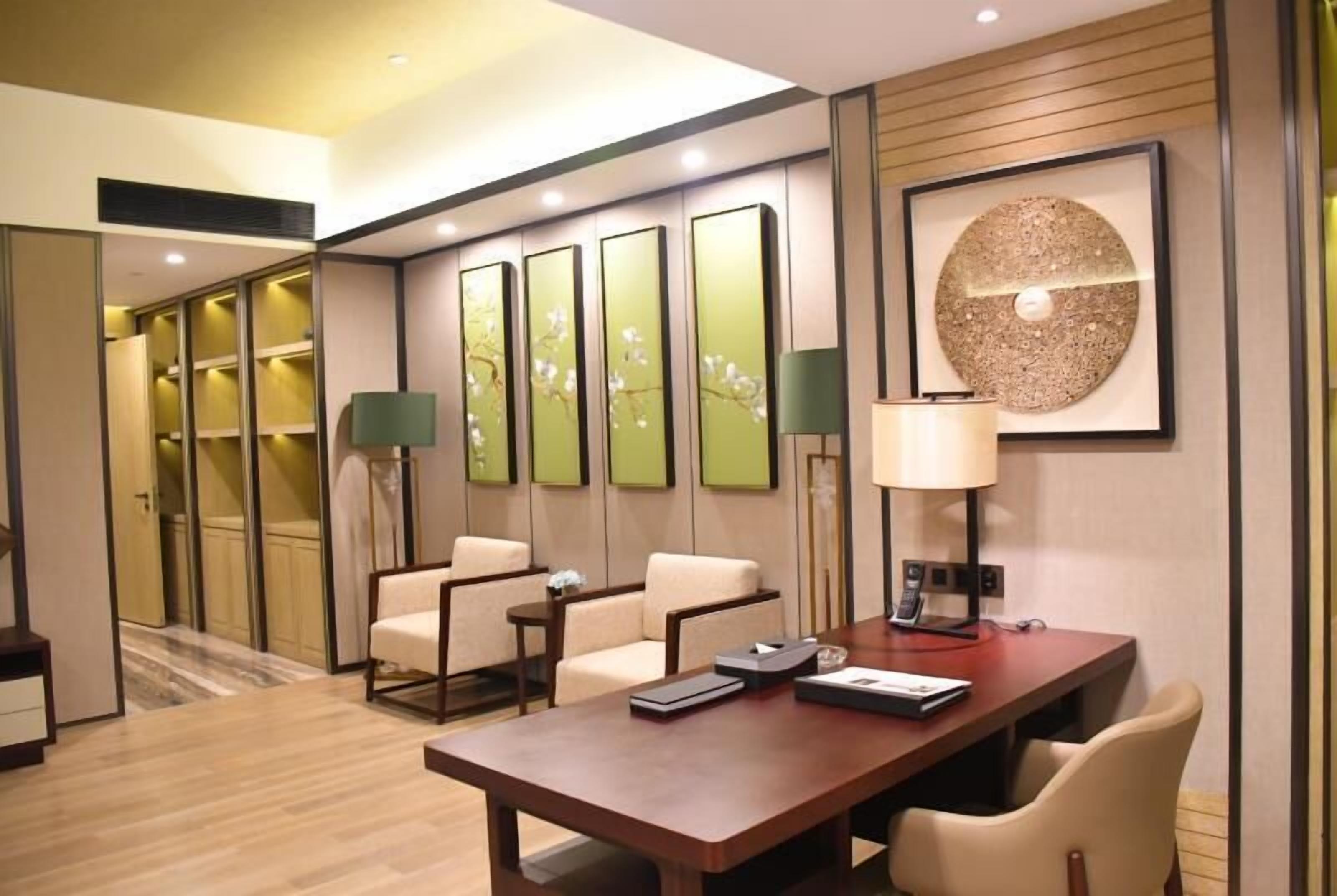 Habitación de hotel con piso de madera, un escritorio con lámpara, una silla y una obra de arte grande en la pared.