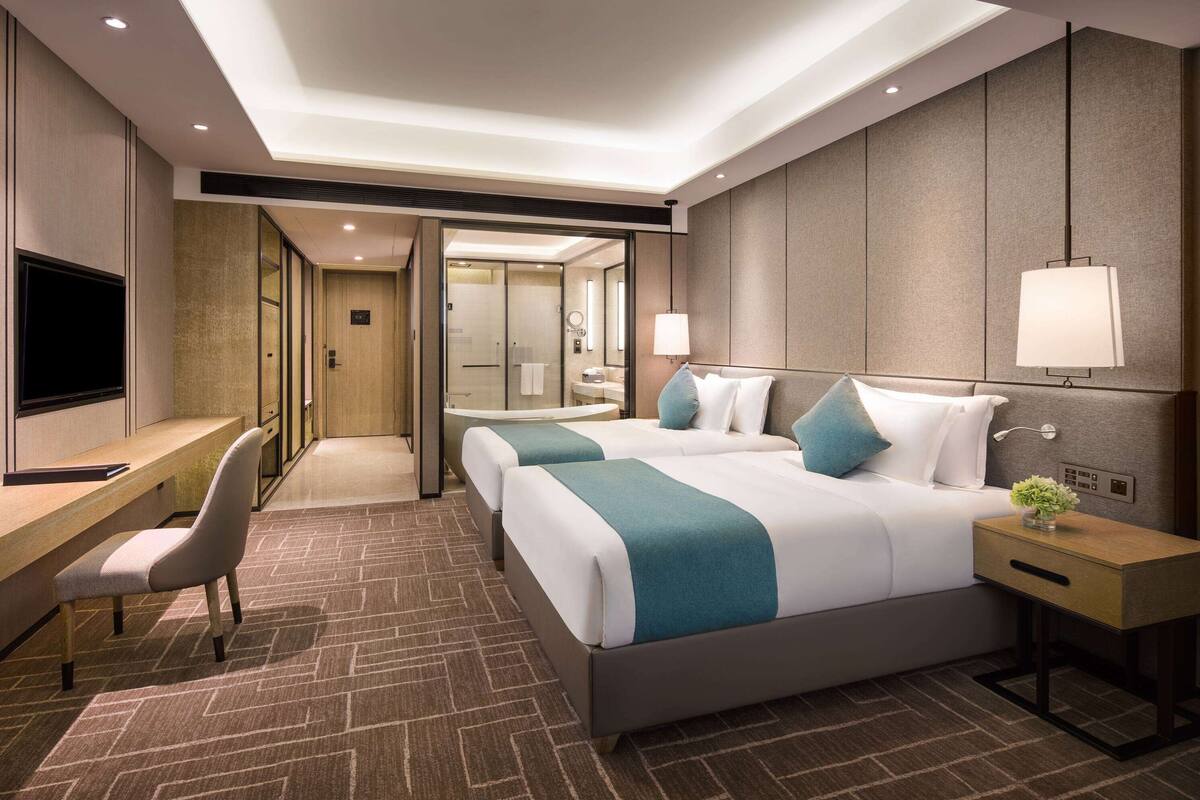 A hotel room with a large bed, a desk, a chair, and a TV.