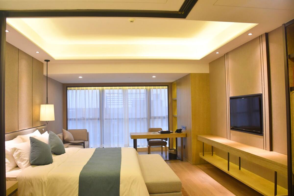 A hotel room with a bed, a desk, a chair, a TV, and a window with curtains.