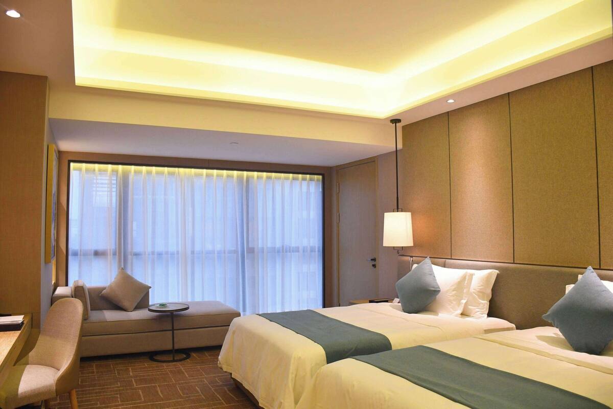 A hotel room with two beds, a sofa, a small table, and a lamp.